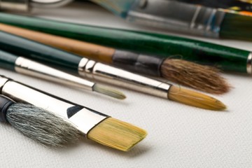 Artistic art supply utensils with brushes on white canvas background with selective focus