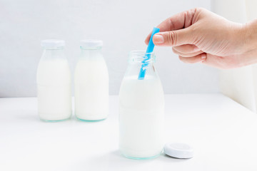 Woman hand holding a blue suck straws in glass bottle of milk on white table background for food and healthy concept. with copy space for text.