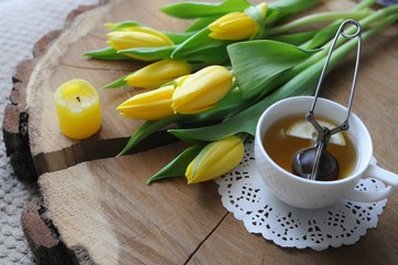 A cup of tea with tea pot with yellow tulips on wooden table