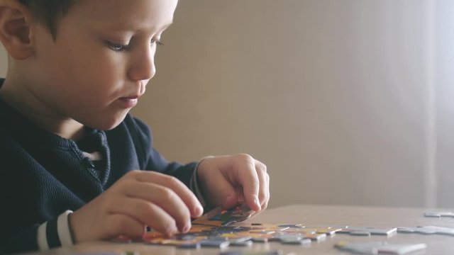 The boy enthusiastically collects puzzles at the table. Close-up