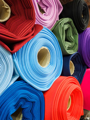Rolls of bright multicolored fabric close-up. Many different fabrics are rolled up and lying on the shelves. Samples of different natural fabrics in the warehouse of the fabric factory