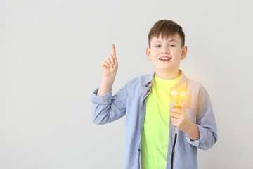 Cute little schoolboy with glowing light bulb on grey background