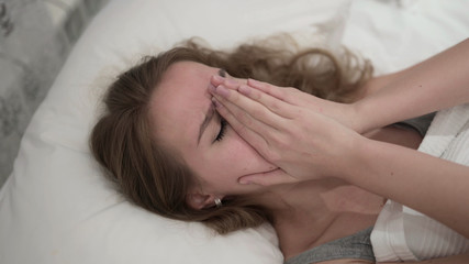 Fototapeta na wymiar Crying Young Woman Hiding Face with Hands in Bed