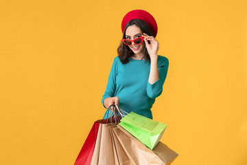 Beautiful young woman with shopping bags on color background