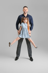 Father and his little daughter dancing against grey background