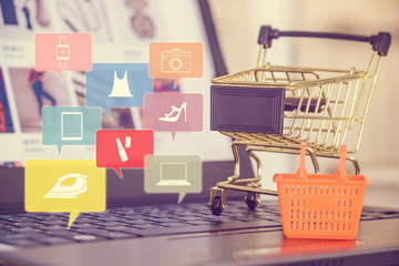 Online shopping / e-commerce and customer experience concept : Shopping cart and a plastic basket on a laptop computer keyboard, depicts consumers / buyers buy / purchase goods and service from home - obrazy, fototapety, plakaty