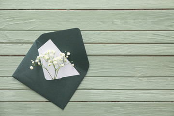 Envelope with card and flowers on color wooden background