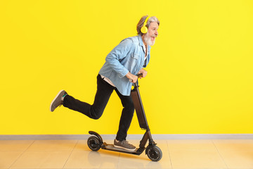 Happy elderly man with kick scooter and headphones near color wall © Pixel-Shot