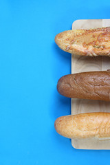 three baguettes on wooden cutting board on blue background flat lay. Vertical image