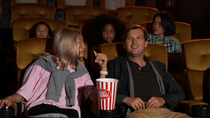Audience walking to seats in the movie theater, watching film and eating popcorn.