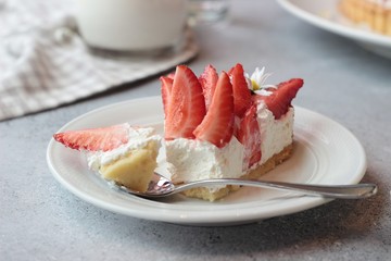 A piece of delicious tart with cream and fresh strawberries on a white plate, light grey stone background.