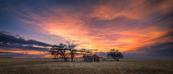 Old abandoned farmhouse on the great plains at sunset. The sky is very dramatic with lots of color. 