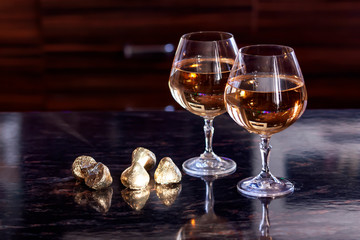 Two glasses of white wine and candy wrapped in gold on a dark background
