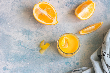 Jar of homemade lemon curd or custard and fresh lemons on a light blue stone background. Selective focus. Top view.