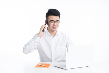 A young Asian man is using his mobile phone and laptop