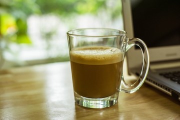 Hot coffee and  milk foam cup on wood table work with laptop notebook computer.