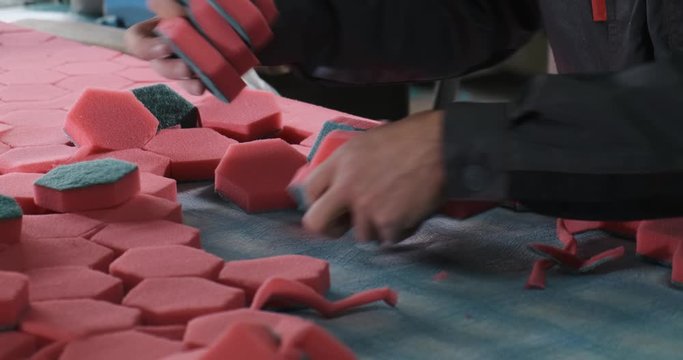 Male worker at factory operates conveyor belt, producing synthetic household products, dish-washing sponges and plumbing cleaners, hexagonal, worker manually removes finished products from conveyor