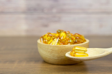A pile of cod liver oil capsule in a cup and wooden spoon. Dietary supplement for health-care concepts.