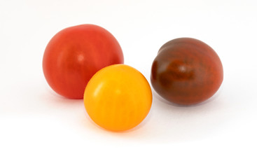 Three multi-colored cherry tomatoes on a white background. Yellow, red, brown