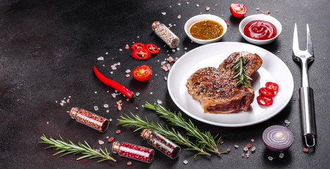 Fresh delicious juicy steak on the bones with vegetables and spices against a dark background