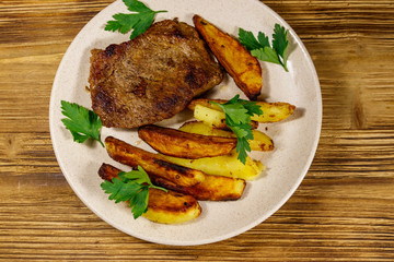 Fried beef steak with potato wedges on wooden table. Top view