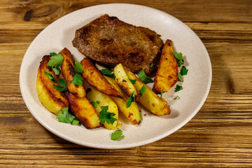 Fried beef steak with potato wedges on wooden table