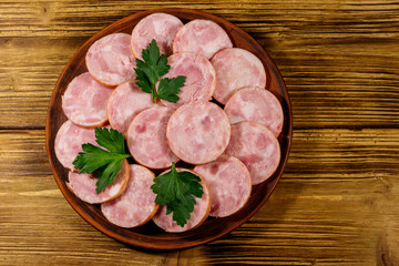 Ham sausage on a plate on wooden table. Top view