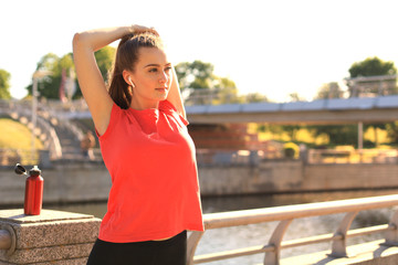 Beautiful young woman in sports clothing stretching her arms and looking concentrated while standing on the bridge.