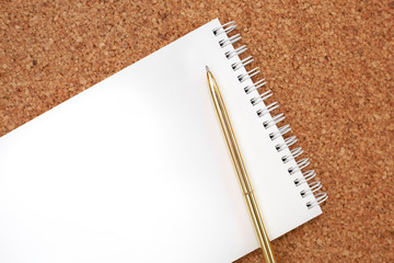 Gold pen on white notebook on cork background