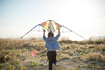 active little kid with color kite running toward bright sunset and sea coast trying to free fly