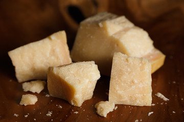 Pieces of parmesan or parmigiano reggiano cheese on a wooden board. Parmesan cheese uses in pasta, risotto and salads. Close-up.