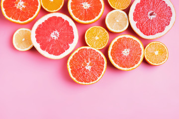 Flat lay composition with halves of different citrus fruits on pink background.