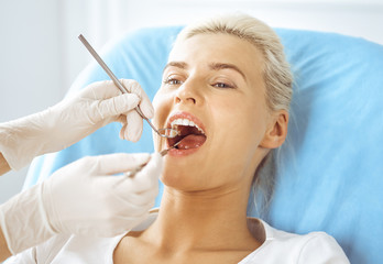 Smiling blonde woman examined by dentist at dental clinic. Healthy teeth and medicine concept