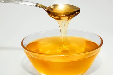 Honey drips from a from a  teaspoon into a glass bowl. Young therapeutic honey. Sweet dessert.