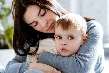 young mother hugs her little son in front of the window