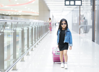 Asian child cute or kid girl walk dragging luggage or baggage and pink suitcase with wear sunglasses and denim shirt or jeans on walkway in airport for holiday travel relax and summer vacation trip