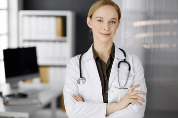 Cheerful smiling female doctor standing in clinic. Portrait of friendly physician woman. Perfect...