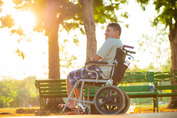 Young disabled asian man sitting on wheelchair in city park sunset light