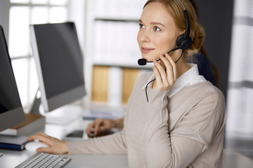 Businesswoman talking by headset while sitting in office. Call center and diverse people group in business