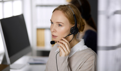 Businesswoman talking by headset while sitting in office. Call center and diverse people group in business