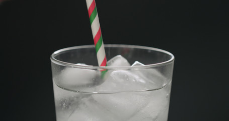 drink with paper straw soda from glass with ice cubes on black background closeup
