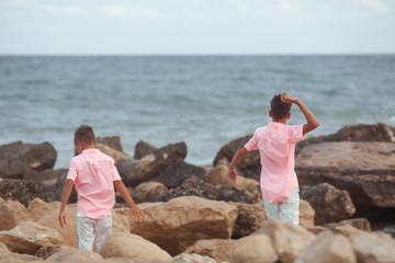 Two brothers play on the seashore, they are dressed in coral shirts and throw stones in the water, summer