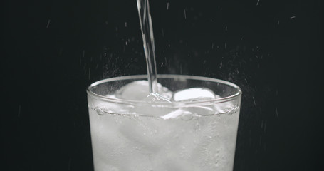 pour soda in glass with ice cubes on black background closeup