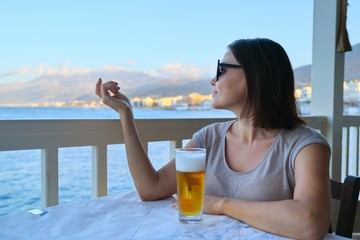 Mature woman resting sitting in sea cafe with cold glass of beer