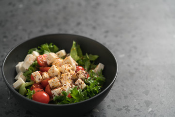Healthy light salad with cherry tomatoes, mozzarella and frisee in black bowl on concrete surface