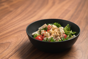 Healthy light salad with cherry tomatoes, mozzarella and frisee in black bowl on walnut surface