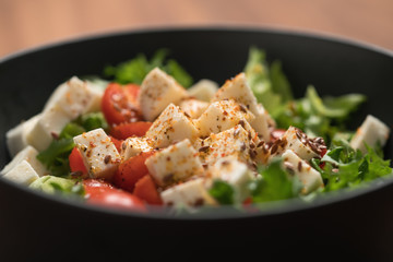 Healthy light salad with cherry tomatoes, mozzarella and frisee in black bowl on walnut surface...