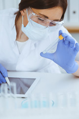 Close-up of professional female scientist in protective eyeglasses making experiment with reagents...