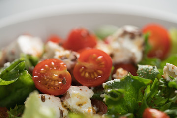 Healthy light salad with cherry tomatoes, mozzarella and frisee in white bowl closeup