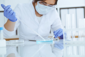 Close-up of professional female scientist in protective eyeglasses making experiment with reagents in laboratory. Medicine and research concept